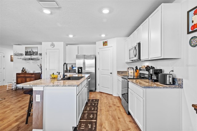 kitchen with white cabinets, appliances with stainless steel finishes, a center island with sink, and sink