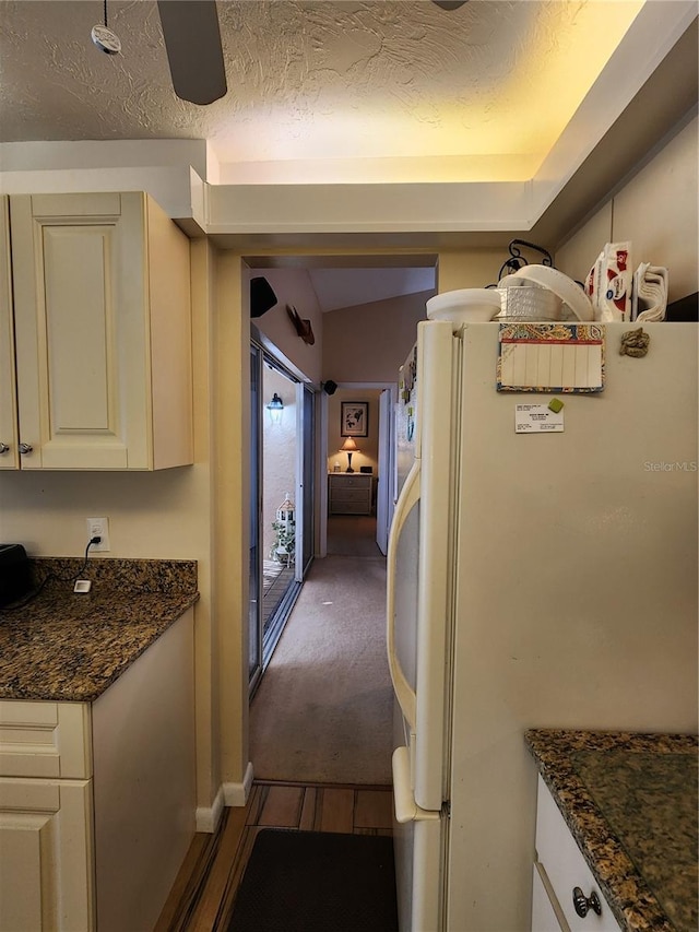 kitchen with white refrigerator, dark stone countertops, lofted ceiling, and dark carpet