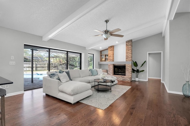 living room with a textured ceiling, vaulted ceiling with beams, ceiling fan, dark hardwood / wood-style floors, and a brick fireplace