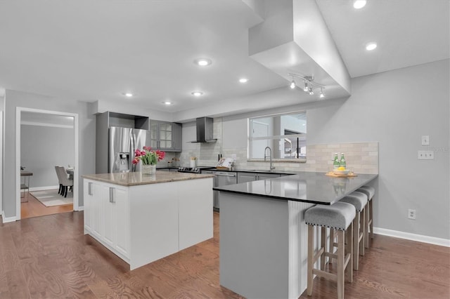 kitchen featuring a kitchen island, wood-type flooring, sink, appliances with stainless steel finishes, and wall chimney exhaust hood