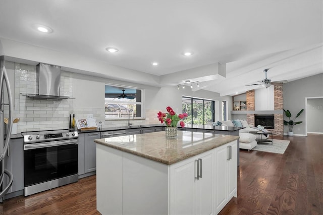 kitchen featuring stainless steel electric range oven, a brick fireplace, tasteful backsplash, wall chimney range hood, and vaulted ceiling