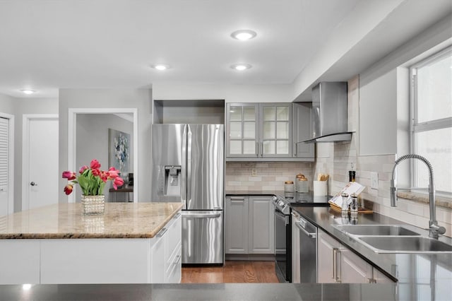 kitchen featuring appliances with stainless steel finishes, wall chimney exhaust hood, tasteful backsplash, sink, and gray cabinetry