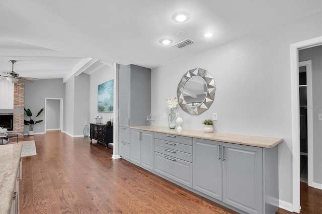 interior space with ceiling fan, gray cabinetry, lofted ceiling, a fireplace, and wood-type flooring