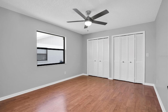 unfurnished bedroom featuring ceiling fan, two closets, a textured ceiling, and wood-type flooring