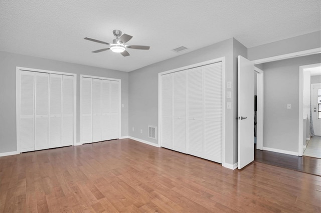 unfurnished bedroom with ceiling fan, a textured ceiling, hardwood / wood-style floors, and multiple closets