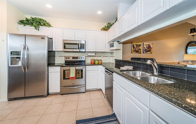 kitchen with white cabinets, sink, dark stone countertops, appliances with stainless steel finishes, and light tile patterned flooring