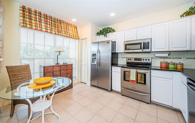 kitchen with backsplash, light tile patterned flooring, white cabinets, and stainless steel appliances