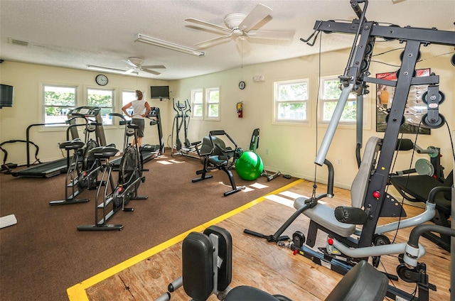 gym featuring a textured ceiling, ceiling fan, and a healthy amount of sunlight