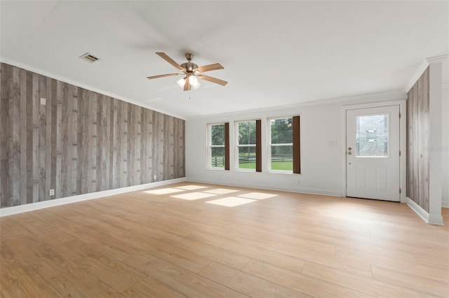 unfurnished living room with ceiling fan, wood walls, light wood-type flooring, and ornamental molding