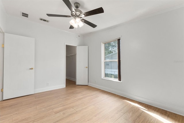 unfurnished bedroom with ceiling fan, light hardwood / wood-style floors, a walk in closet, and a closet