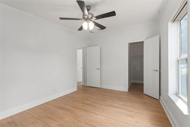 unfurnished bedroom featuring multiple windows, light hardwood / wood-style floors, a spacious closet, and ceiling fan