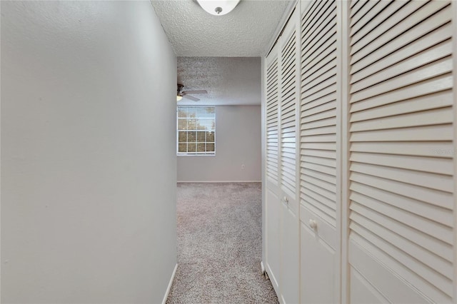 hallway featuring light colored carpet and a textured ceiling