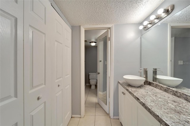 bathroom with tile patterned flooring, a textured ceiling, vanity, and toilet