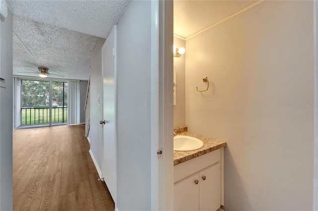 bathroom with ceiling fan, wood-type flooring, a textured ceiling, vanity, and ornamental molding