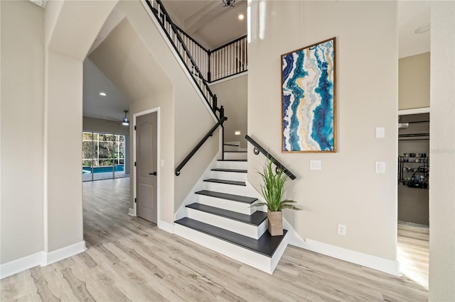 staircase with wood-type flooring, ceiling fan, and a high ceiling