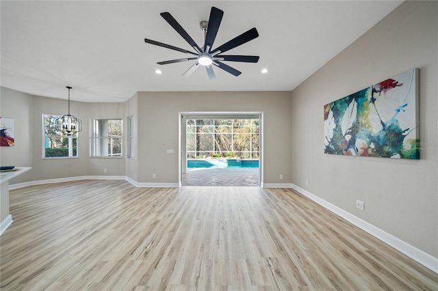 unfurnished living room featuring ceiling fan with notable chandelier and light hardwood / wood-style flooring