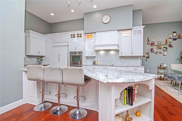 kitchen with paneled fridge, white cabinetry, a breakfast bar area, and light stone counters