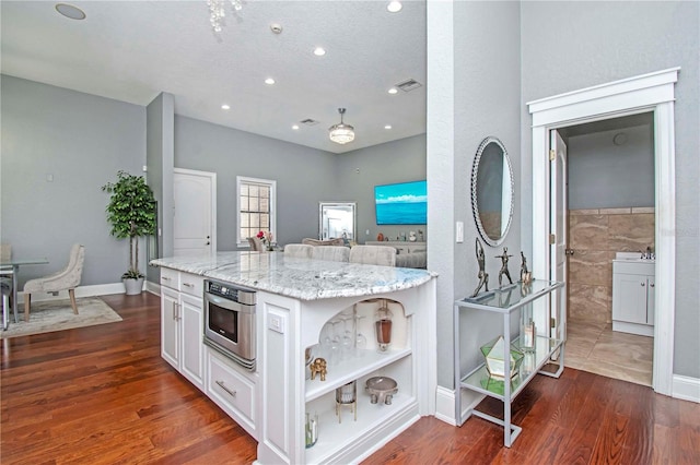 kitchen featuring white cabinets, dark hardwood / wood-style flooring, a kitchen island, and light stone counters