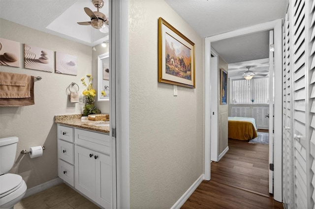 bathroom with ceiling fan, wood-type flooring, a textured ceiling, toilet, and vanity