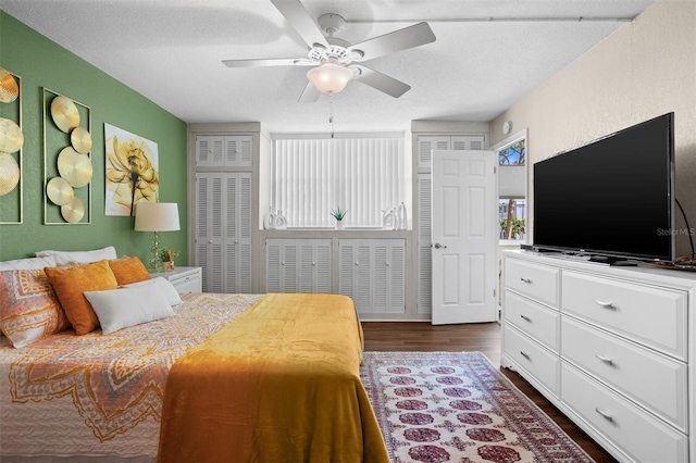 bedroom featuring a textured ceiling, ceiling fan, dark hardwood / wood-style flooring, and two closets