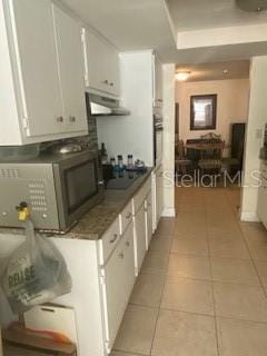 kitchen featuring ventilation hood, light tile patterned flooring, black electric stovetop, and white cabinetry