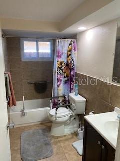 8906 Windsong Ln, Port Richey, FL 34668 - bathroom featuring toilet, vanity, tile patterned floors, shower / bathtub combination with curtain, and tile walls