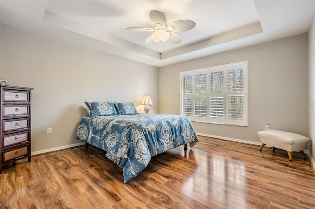 bedroom with hardwood / wood-style flooring, ceiling fan, and a tray ceiling