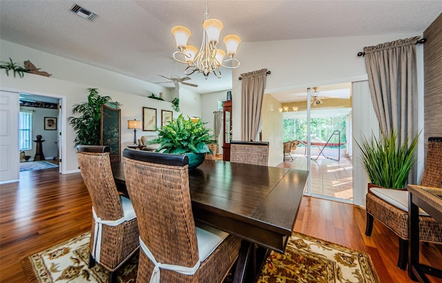 dining room with ceiling fan with notable chandelier, wood-type flooring, a textured ceiling, and vaulted ceiling