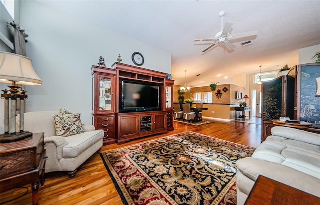 living room featuring a textured ceiling, ceiling fan with notable chandelier, wood-type flooring, and vaulted ceiling