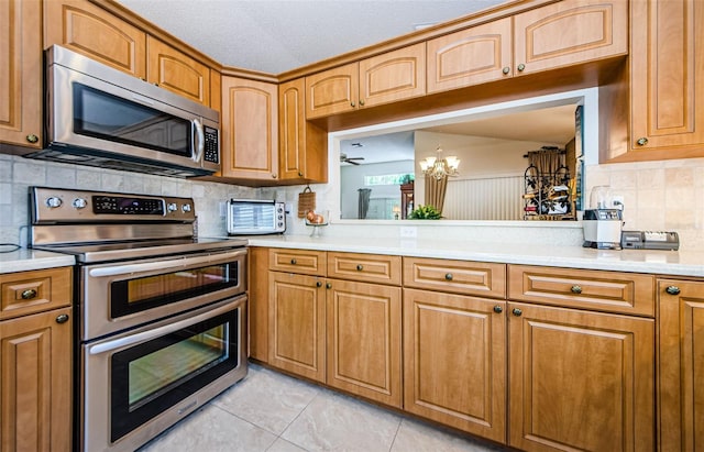 kitchen with appliances with stainless steel finishes, backsplash, a textured ceiling, a chandelier, and light tile patterned flooring