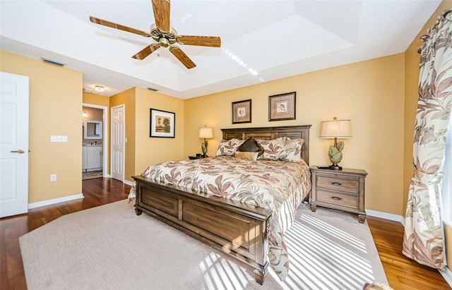 bedroom featuring hardwood / wood-style flooring, ceiling fan, a raised ceiling, and connected bathroom