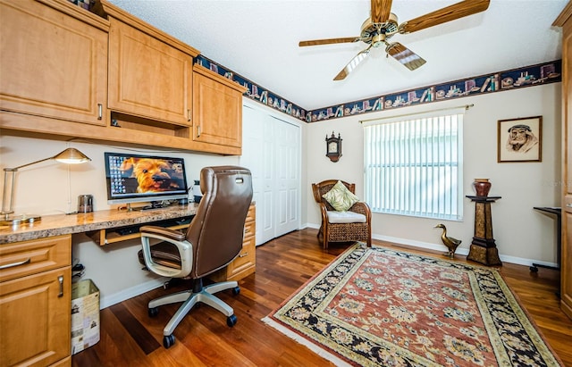 home office with built in desk, ceiling fan, and dark wood-type flooring