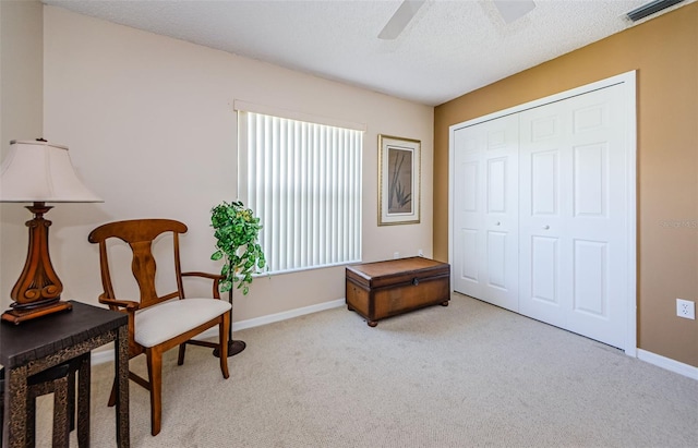 living area featuring light carpet, ceiling fan, and a textured ceiling