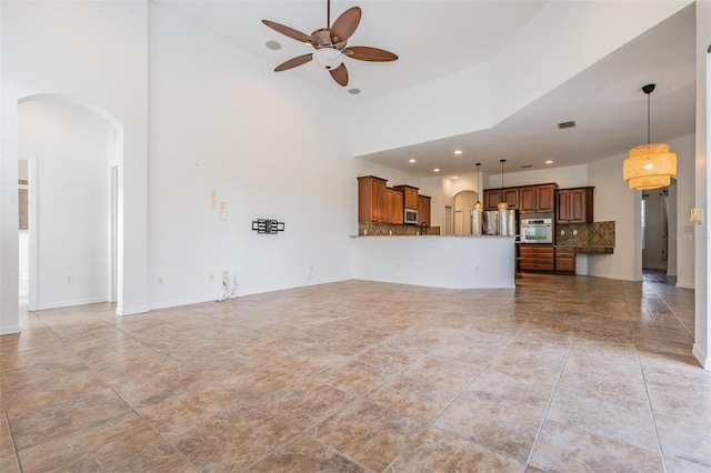 unfurnished living room with ceiling fan and a towering ceiling