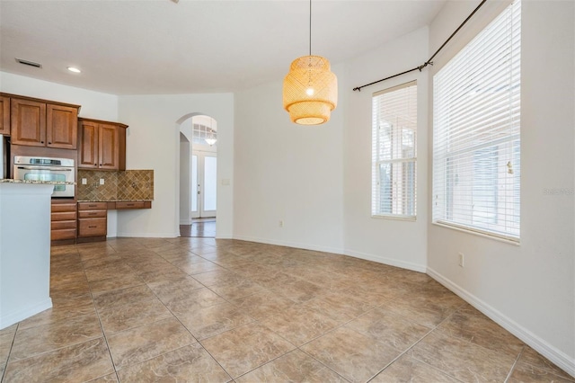 kitchen with light stone countertops, hanging light fixtures, backsplash, oven, and light tile patterned flooring