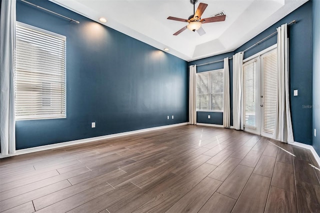 empty room featuring ceiling fan, a healthy amount of sunlight, and a tray ceiling