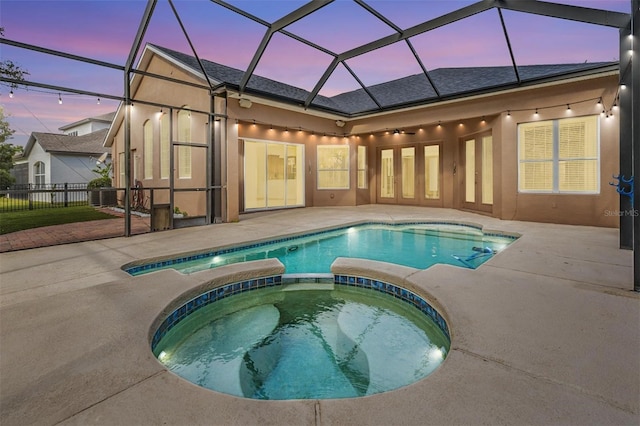 pool at dusk with glass enclosure, an in ground hot tub, and a patio