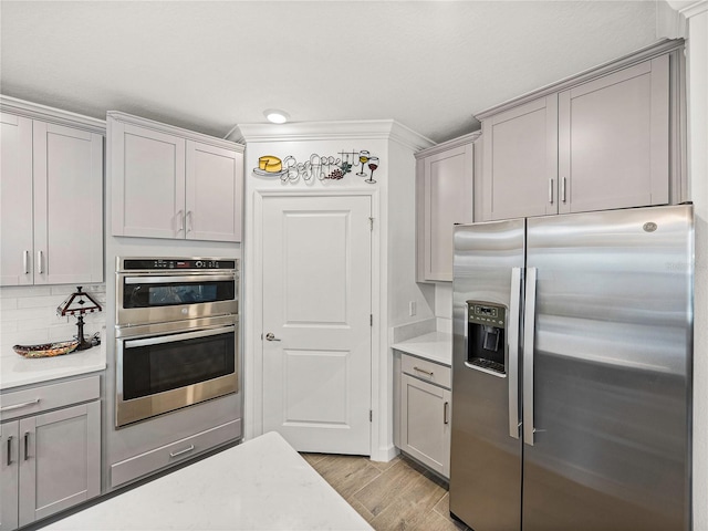 kitchen featuring gray cabinetry, light wood-type flooring, appliances with stainless steel finishes, and tasteful backsplash