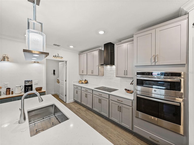 kitchen featuring black electric cooktop, double oven, crown molding, wall chimney range hood, and hardwood / wood-style flooring