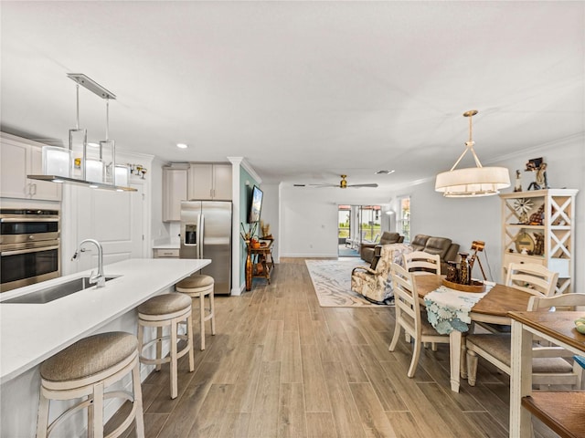 kitchen with sink, light hardwood / wood-style flooring, pendant lighting, a breakfast bar area, and appliances with stainless steel finishes