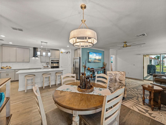 dining room with ceiling fan, sink, ornamental molding, and light wood-type flooring