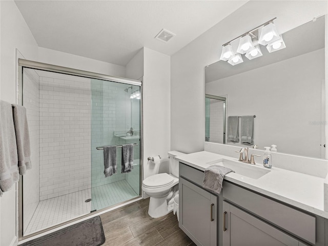 bathroom featuring wood-type flooring, vanity, a shower with shower door, and toilet