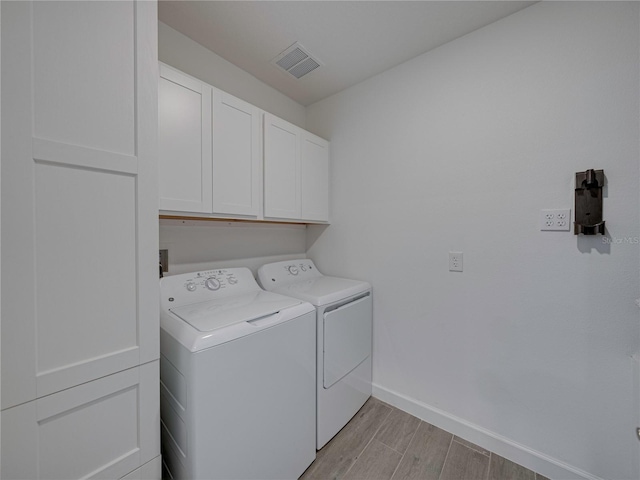 clothes washing area with washing machine and dryer, cabinets, and light hardwood / wood-style floors