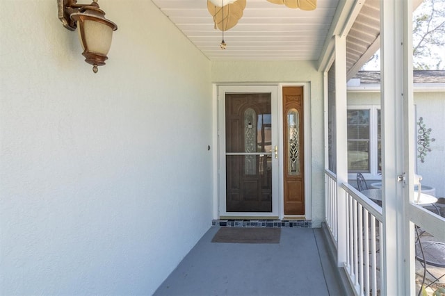 entrance to property with ceiling fan and stucco siding