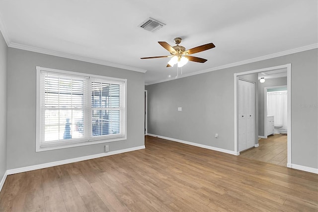 empty room featuring baseboards, wood finished floors, visible vents, and crown molding