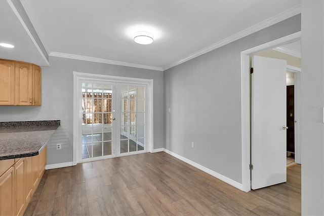 unfurnished dining area featuring french doors, crown molding, baseboards, and wood finished floors