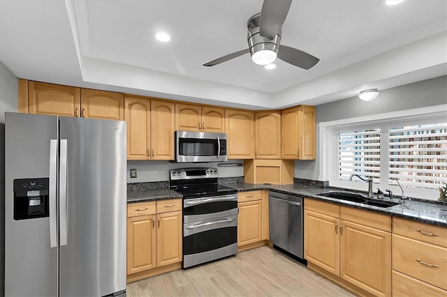 kitchen with light wood-type flooring, a sink, dark stone counters, appliances with stainless steel finishes, and ceiling fan