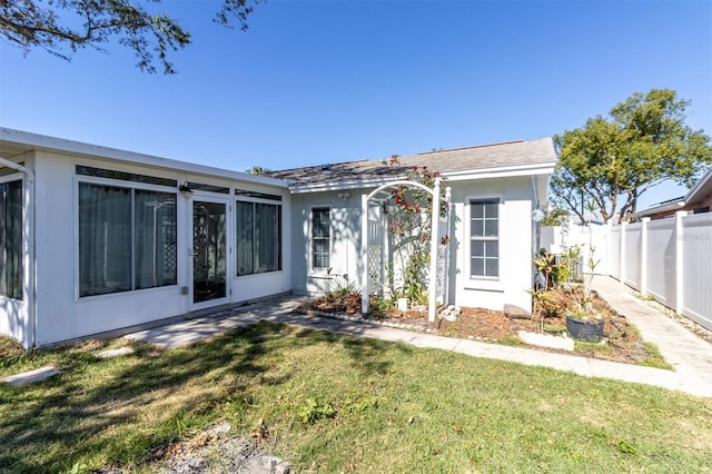 view of front of home with a front yard, a sunroom, fence, and stucco siding