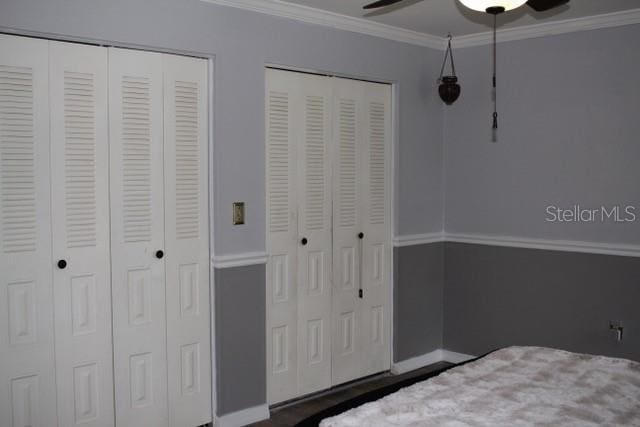 unfurnished bedroom featuring baseboards, ornamental molding, a ceiling fan, and multiple closets