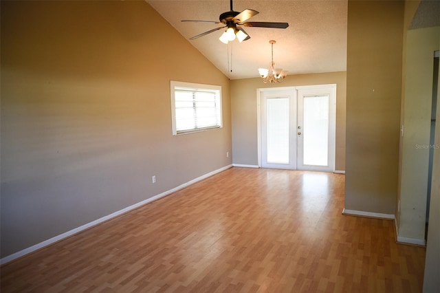 spare room with french doors, light wood-type flooring, ceiling fan with notable chandelier, a textured ceiling, and high vaulted ceiling